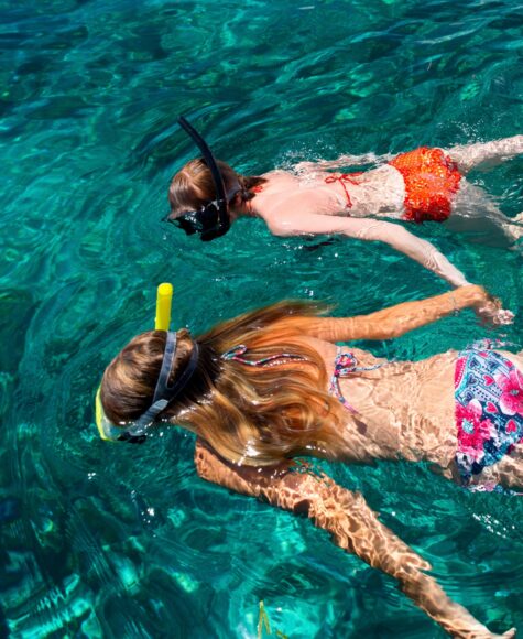 Two girls snorkeling in turquoise water.