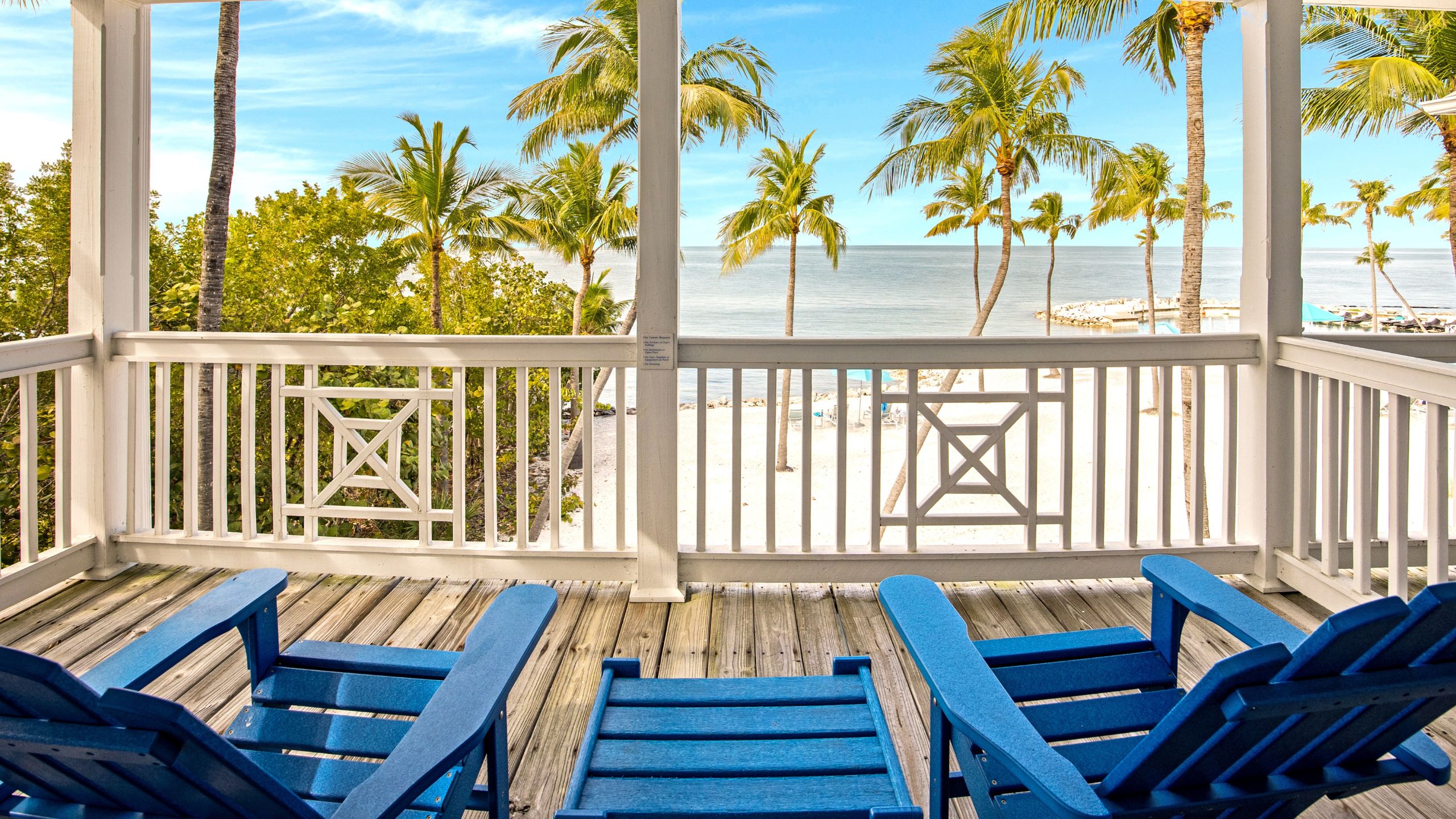 view from balcony with adirondack chairs, beach view with palm trees